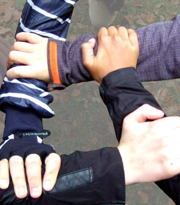 Vier Hände von unterschiedlichen Jungen, die sich an den Handgelenken anfassen und damit einen Kries formen.