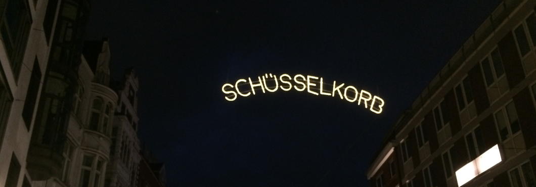 Lichterkette, die zwischen Häusern gespannt ist. Die Lichter bilden den Straßennamen: Schüsselkorb.